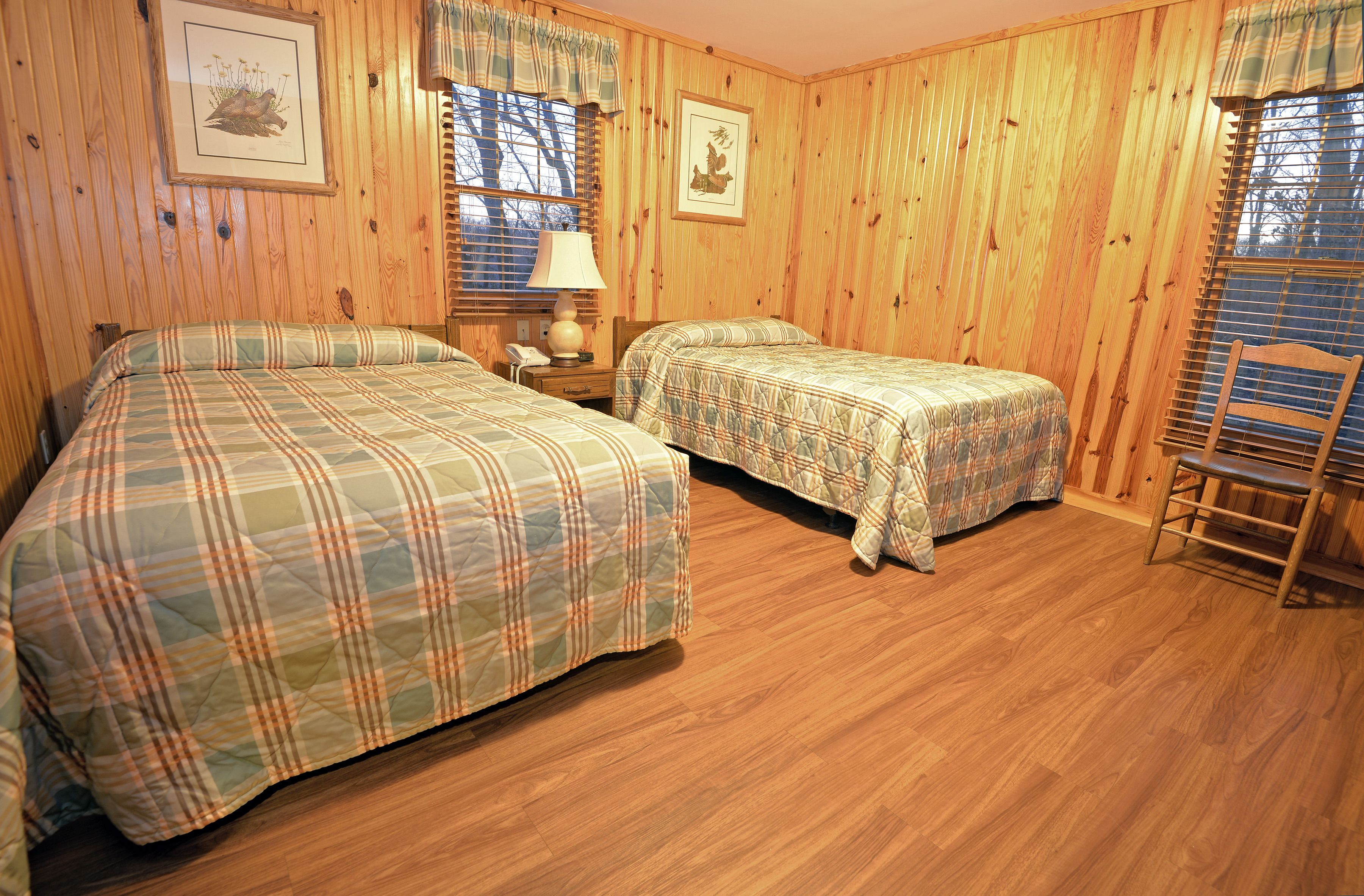 A room with two beds, wooden walls, and a chair.