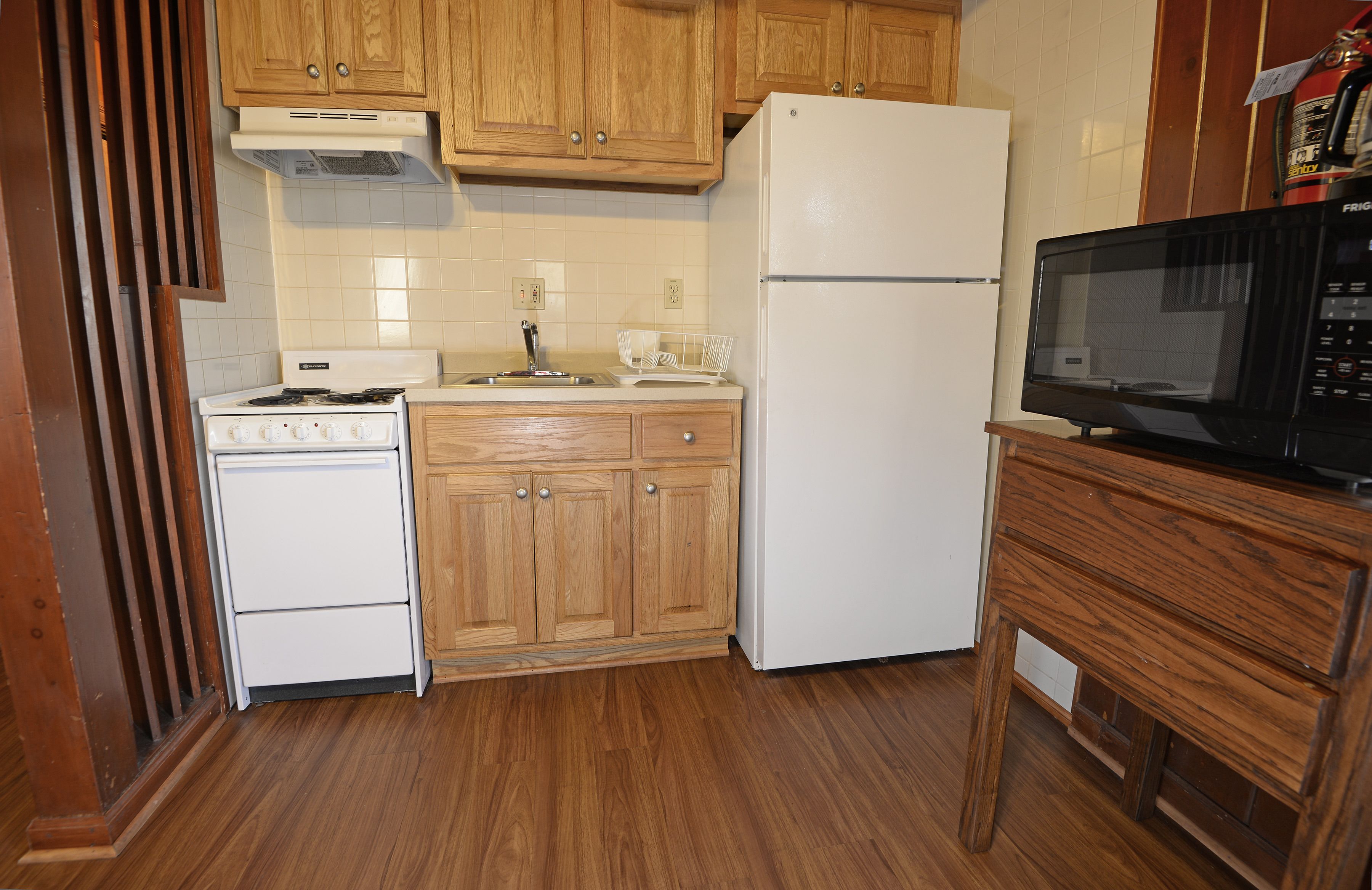 A kitchen with wooden cabinets, a white stove, a white refrigerator, and a black microwave on a wooden table.