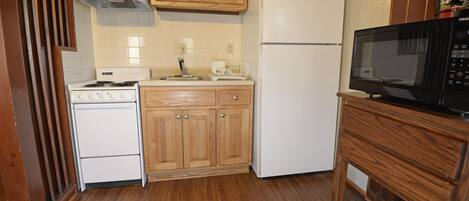 A kitchen with wooden cabinets, a white stove, a white refrigerator, and a black microwave on a wooden table.