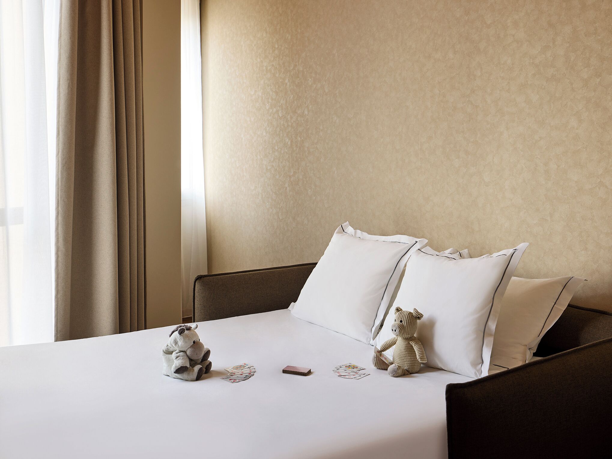 A neatly made bed with white bedding, two pillows, and two stuffed toys on the bed.