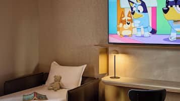 Habitación de hotel con una cama, una silla, una lámpara y un televisor que muestra personajes animados.