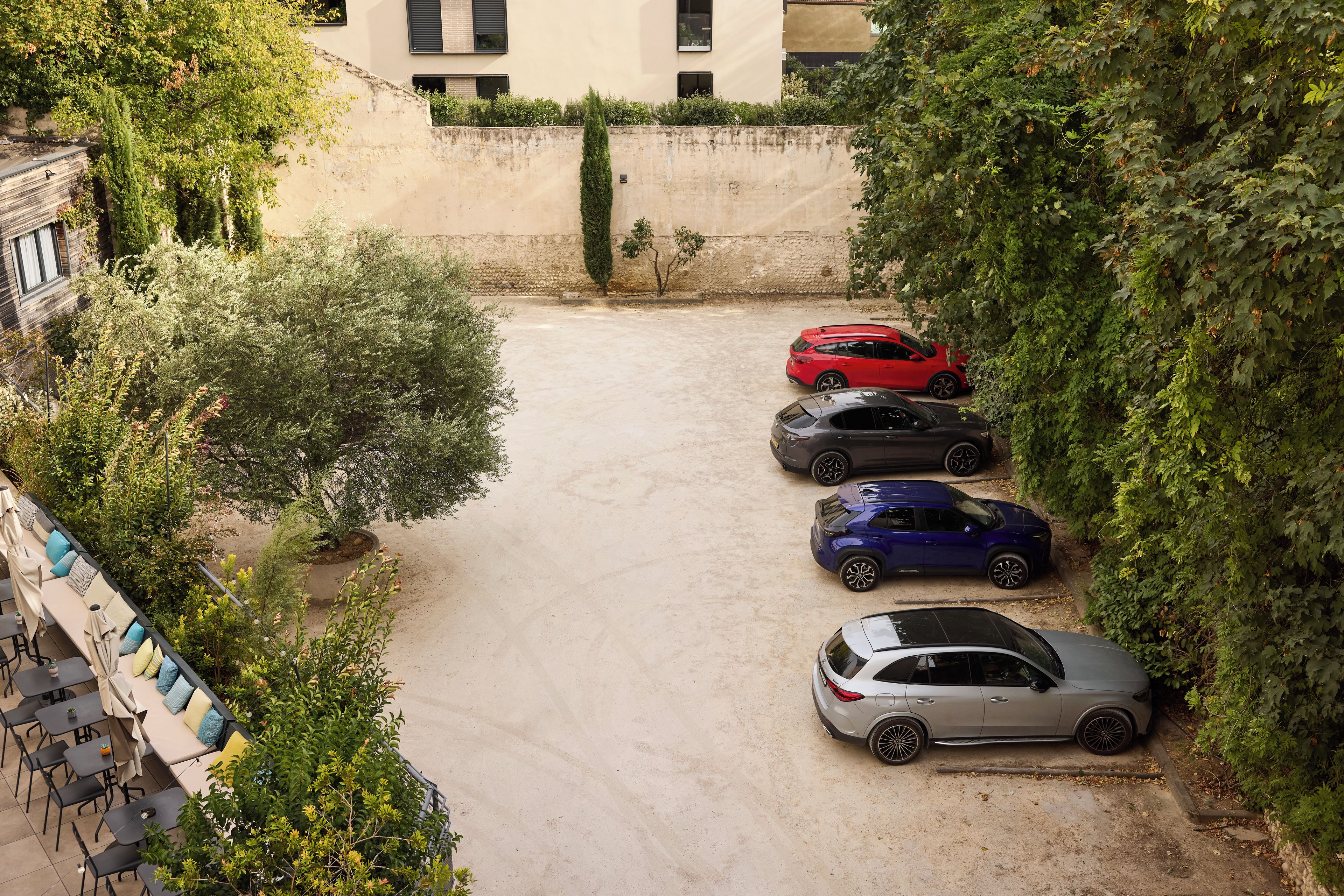 Uma área de estacionamento com cinco carros, rodeada por vegetação e edifícios.