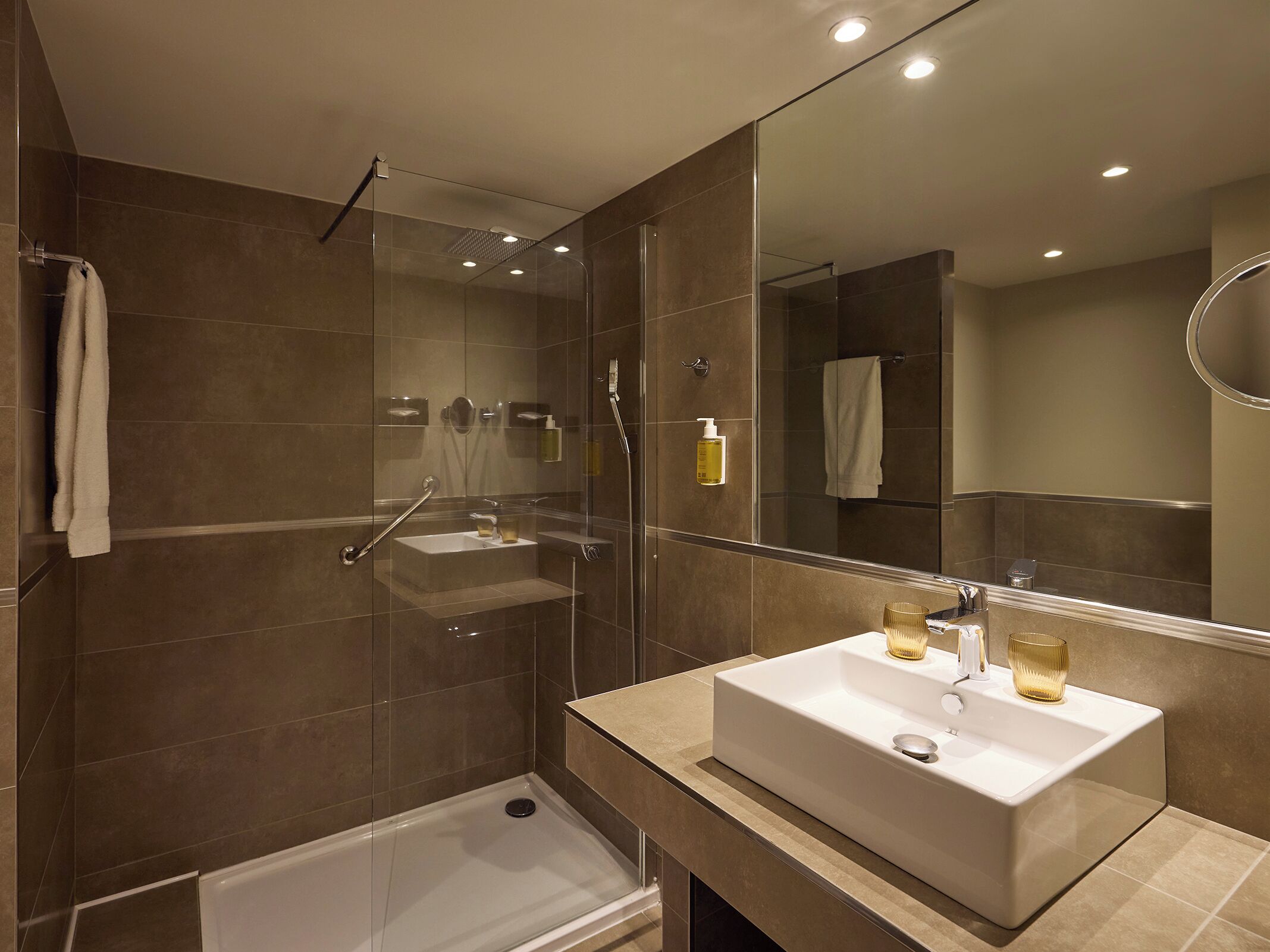 A modern bathroom with a glass-enclosed shower, a white sink, and a large mirror.