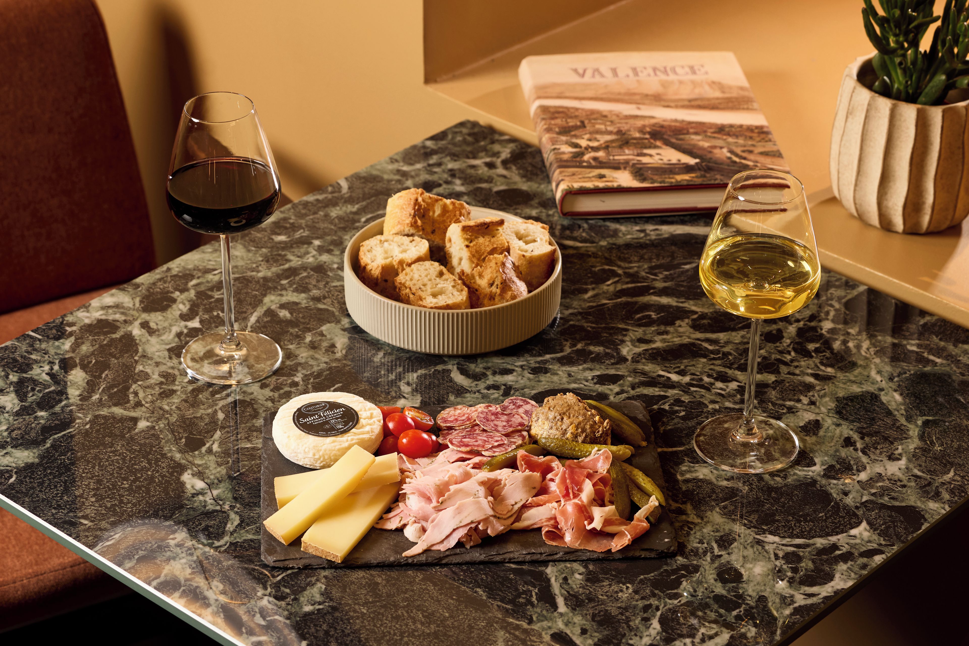 Une table en marbre avec un plateau de fromages, de la charcuterie et deux verres de vin.