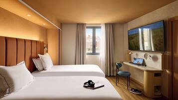Habitación de hotel con dos camas, un escritorio con una computadora portátil, un televisor y una ventana con cortinas.