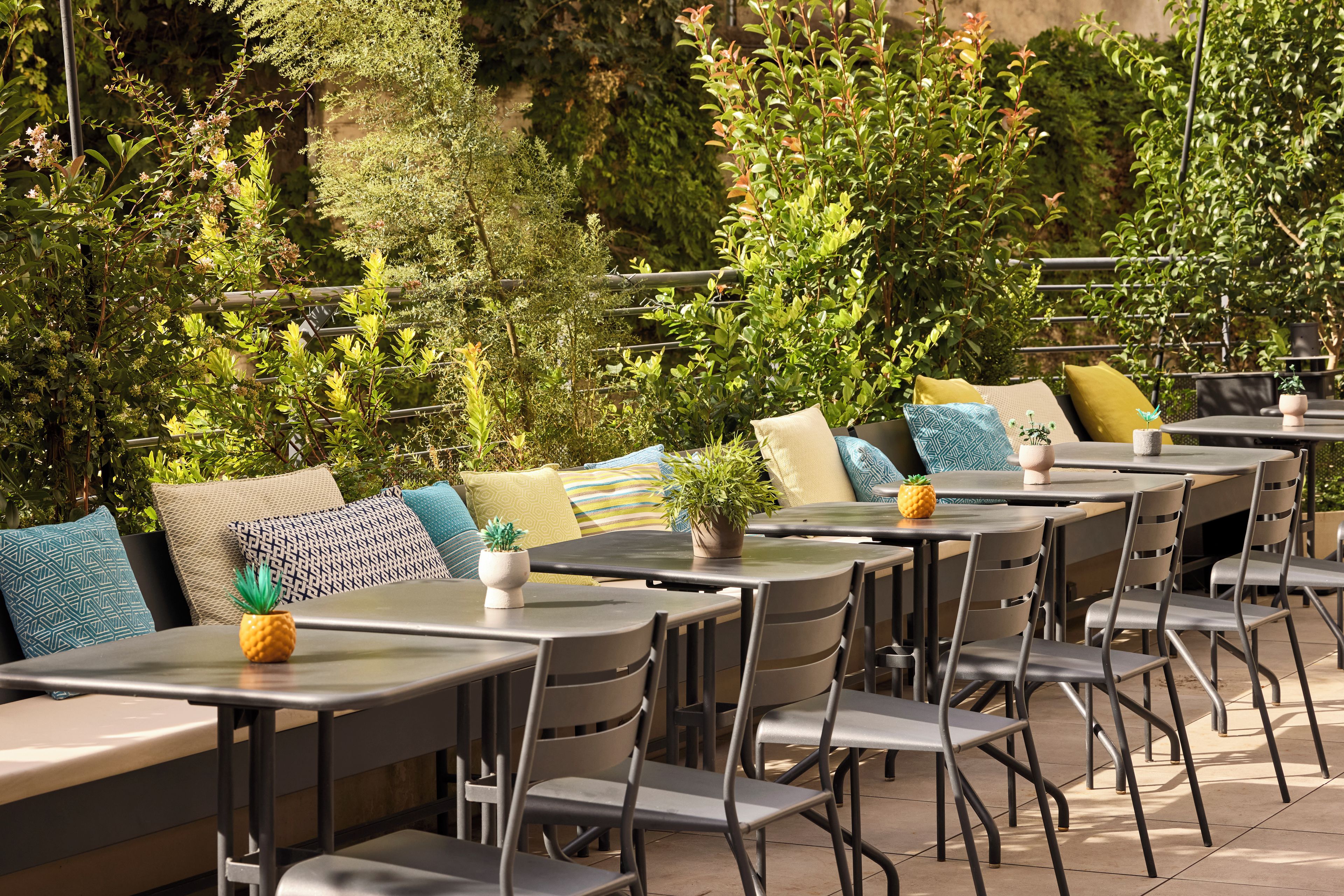 An outdoor seating area with tables and chairs, surrounded by lush greenery.
