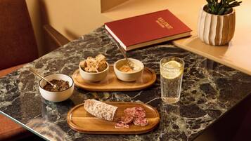 A marble table with a variety of food items including bread, a bowl of what appears to be a spread, a glass of water with a lemon slice, and a book.