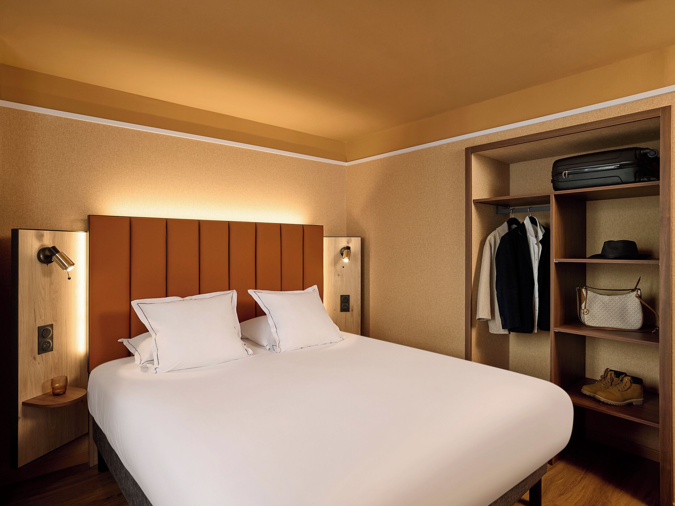 A hotel room with a bed, a wardrobe, and a nightstand with a lamp.