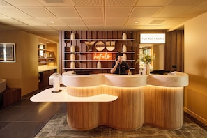 Una recepción de hotel con detalles de madera, un letrero de neón y una recepcionista.