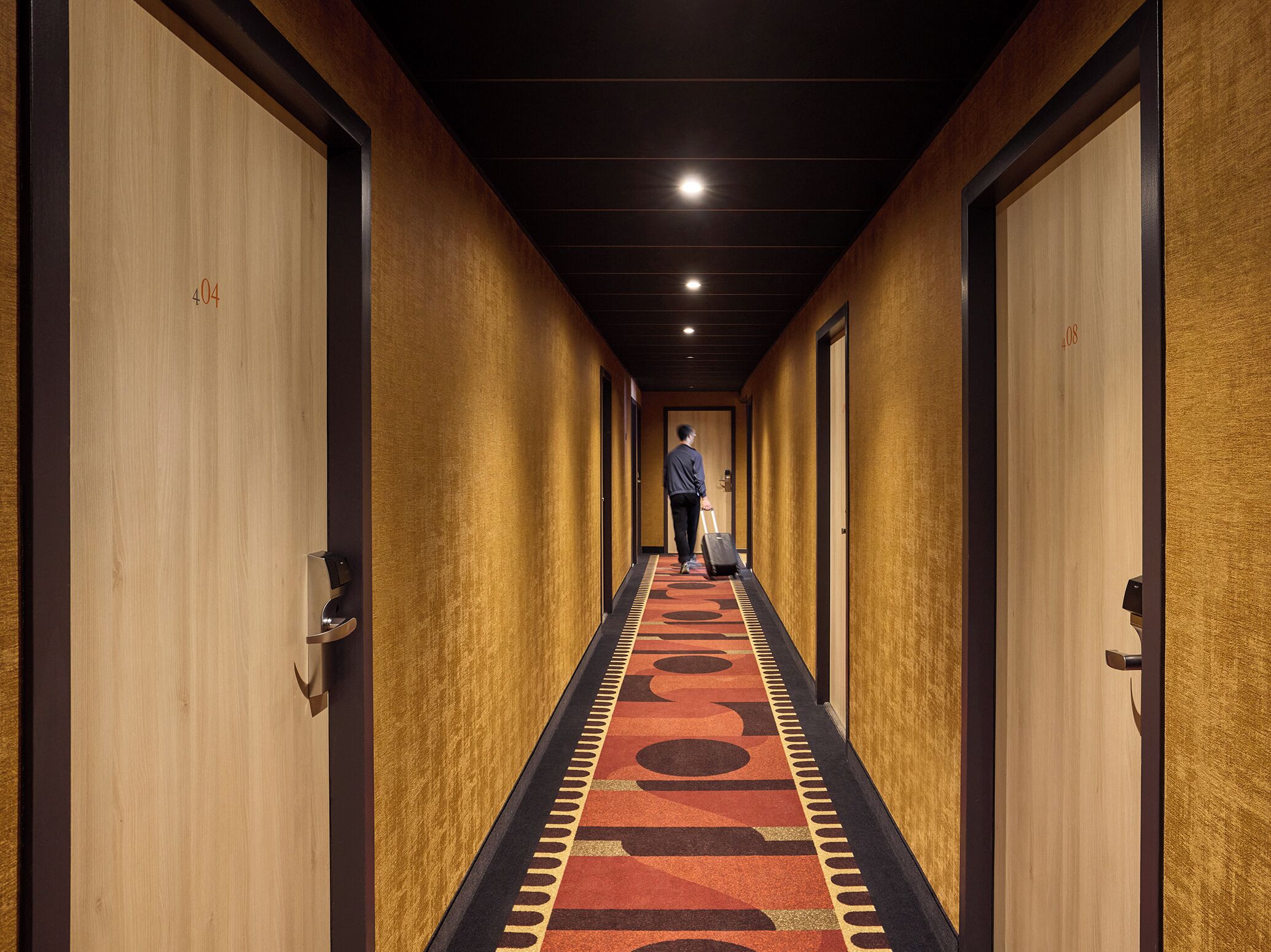A hotel hallway with doors numbered 404 and 108, a person with a suitcase, and a carpet with a geometric pattern.
