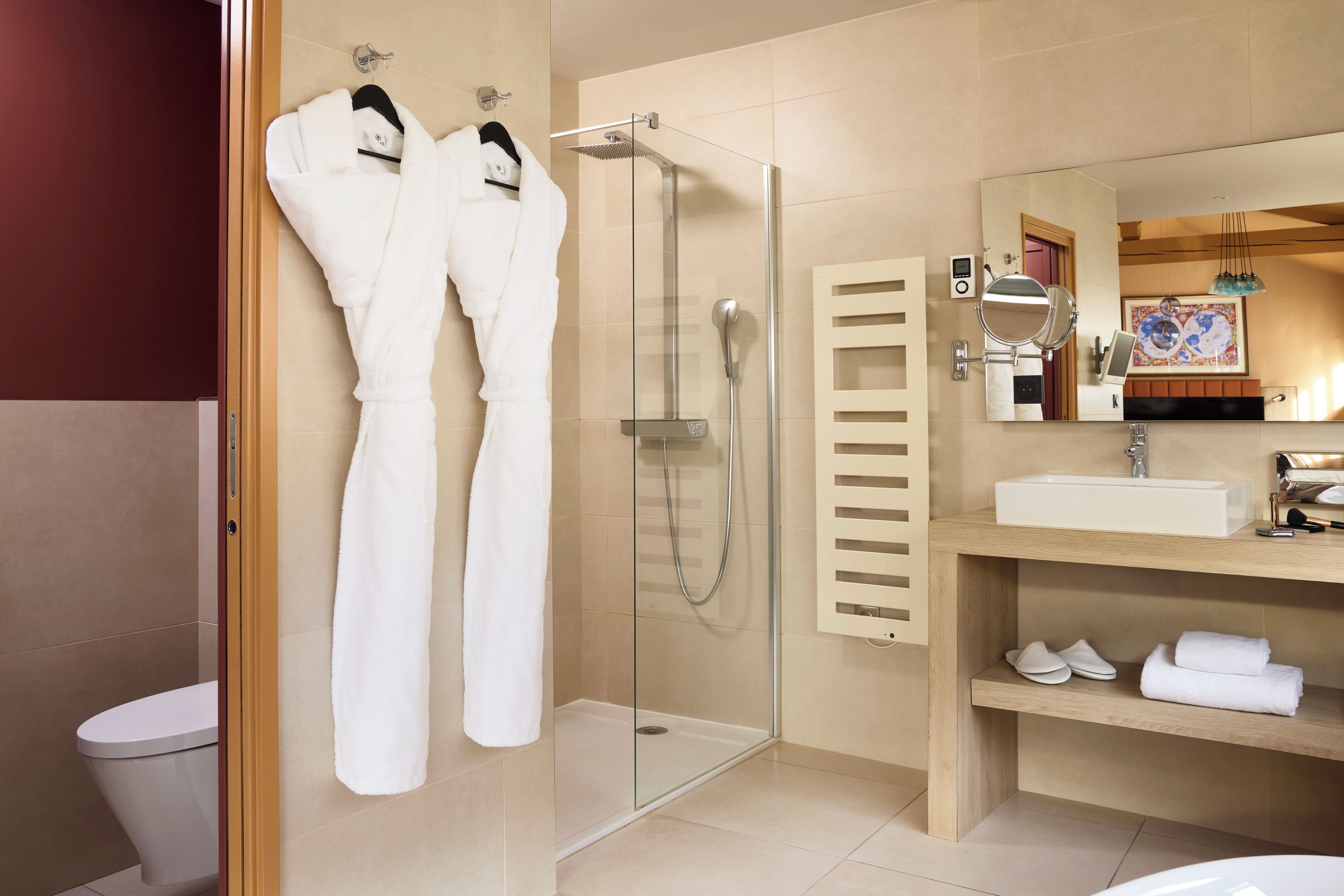 Un baño moderno con ducha envuelta en vidrio, tocador de madera con lavamanos y dos toallas blancas colgadas en un perchero.
