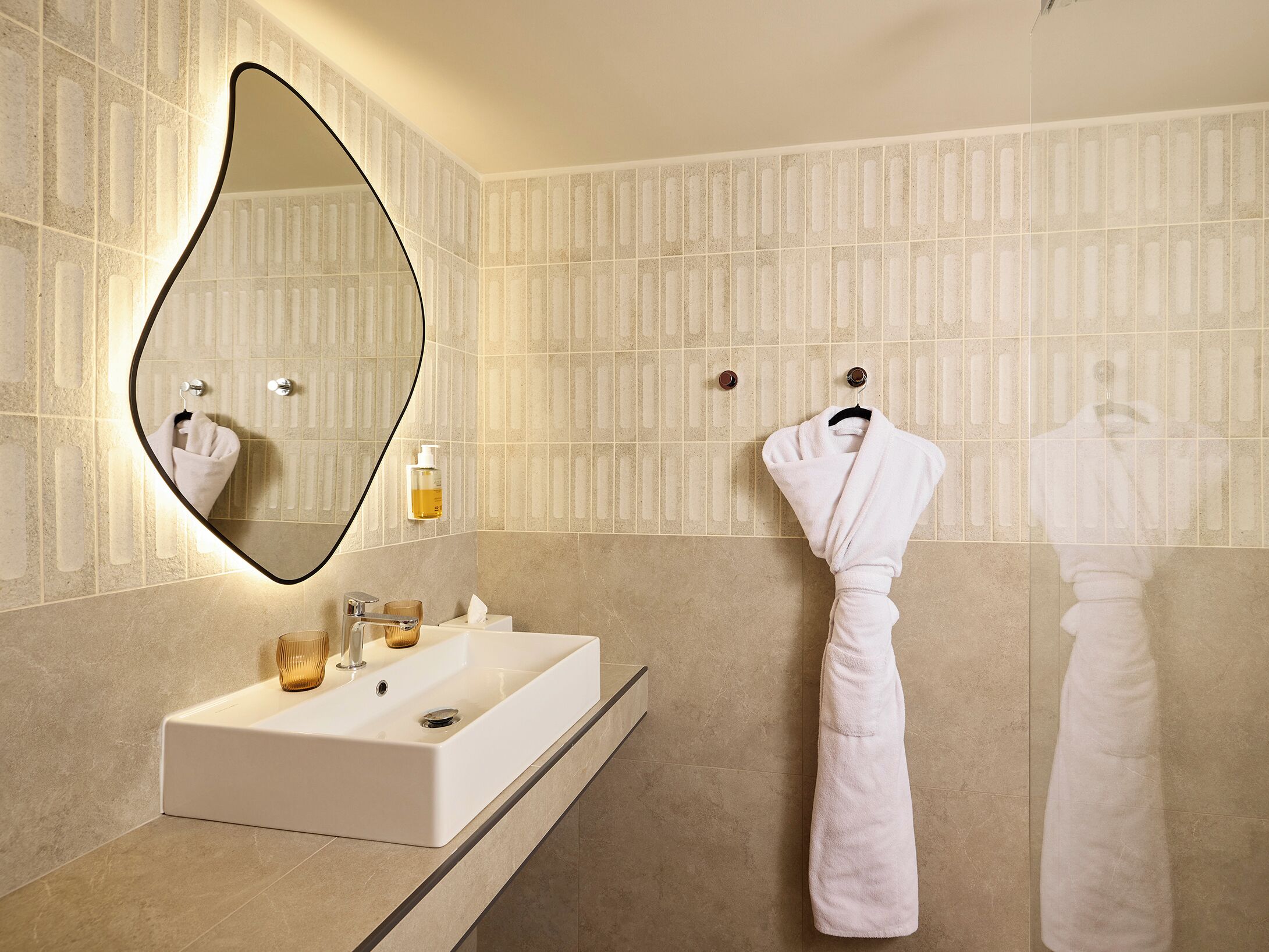 Un baño con un espejo grande, un lavabo y dos toallas colgadas en ganchos.