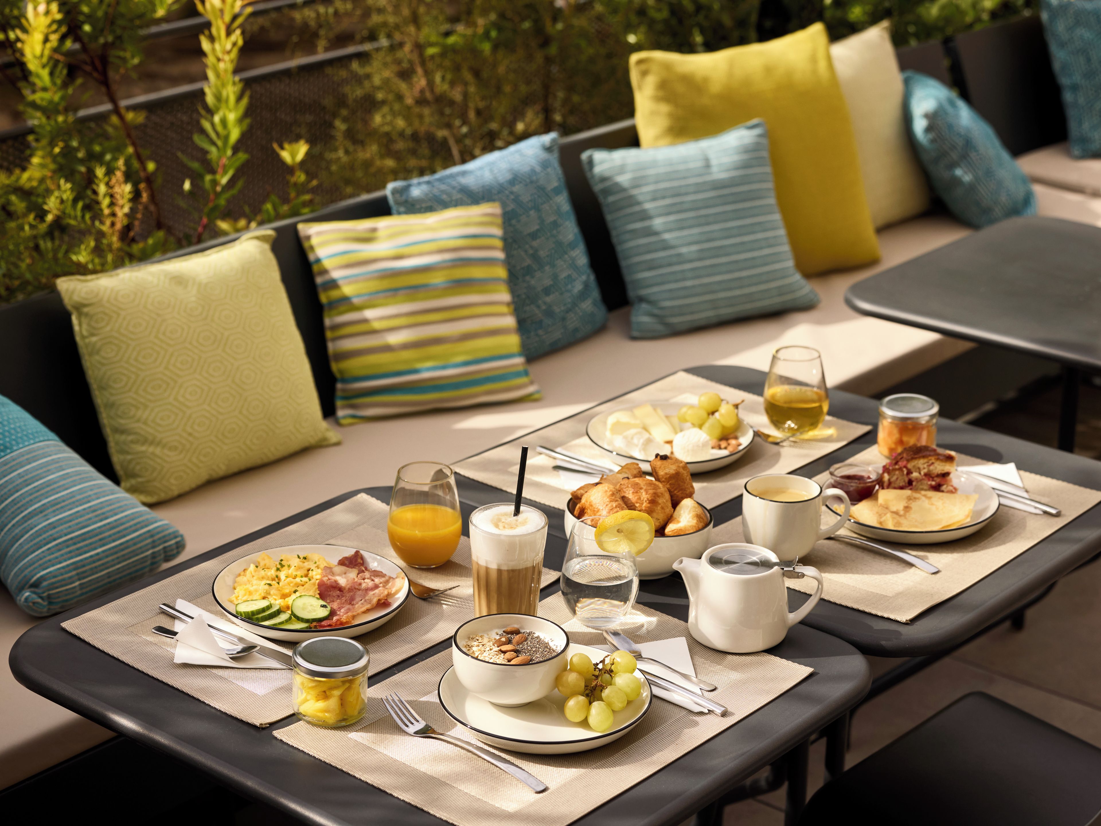 A breakfast setup with a variety of dishes, drinks, and a table set outdoors.