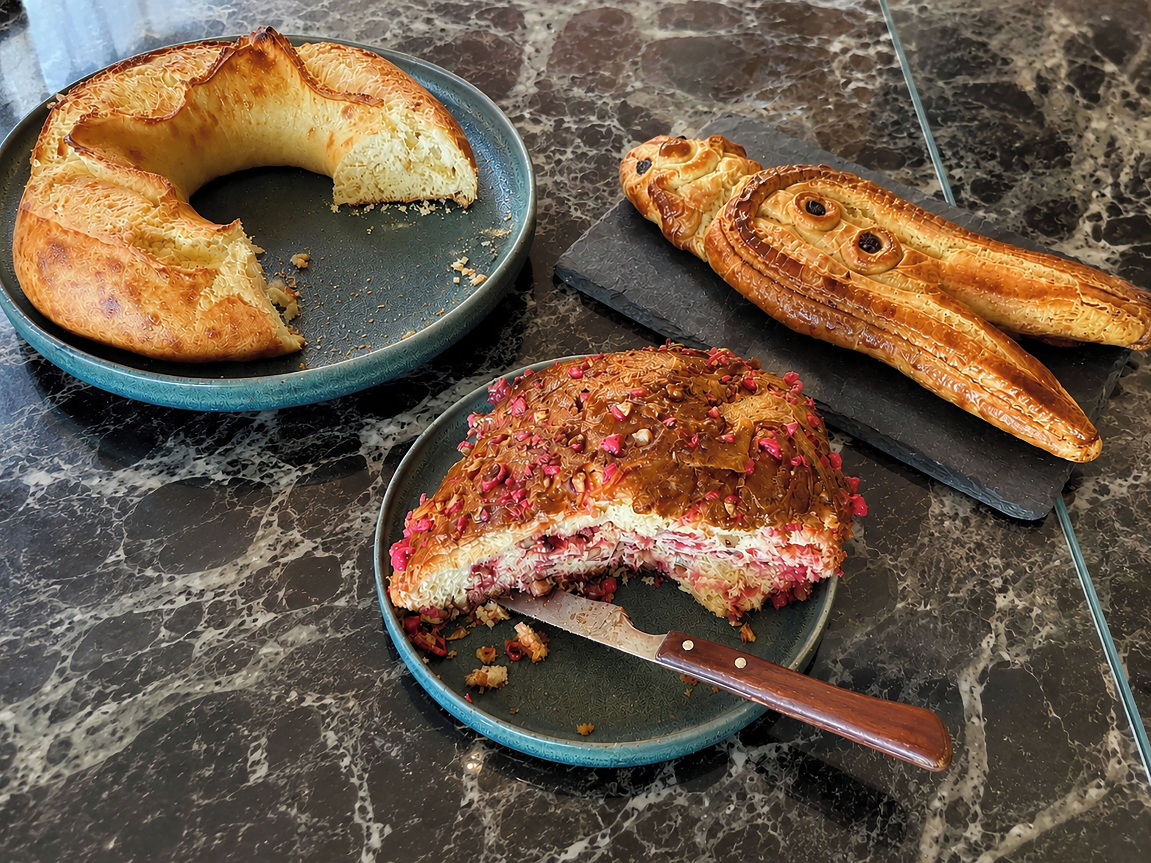 A marble countertop with a cake on a plate and a cake on a plate with a knife.