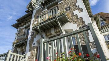 A multi-story building with a stone facade, multiple balconies, and a staircase leading to the entrance.