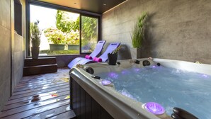 A modern spa area with a hot tub, wooden deck, and potted plants.