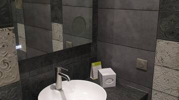 Un baño moderno con un lavamanos blanco, baldosas oscuras y un espejo.