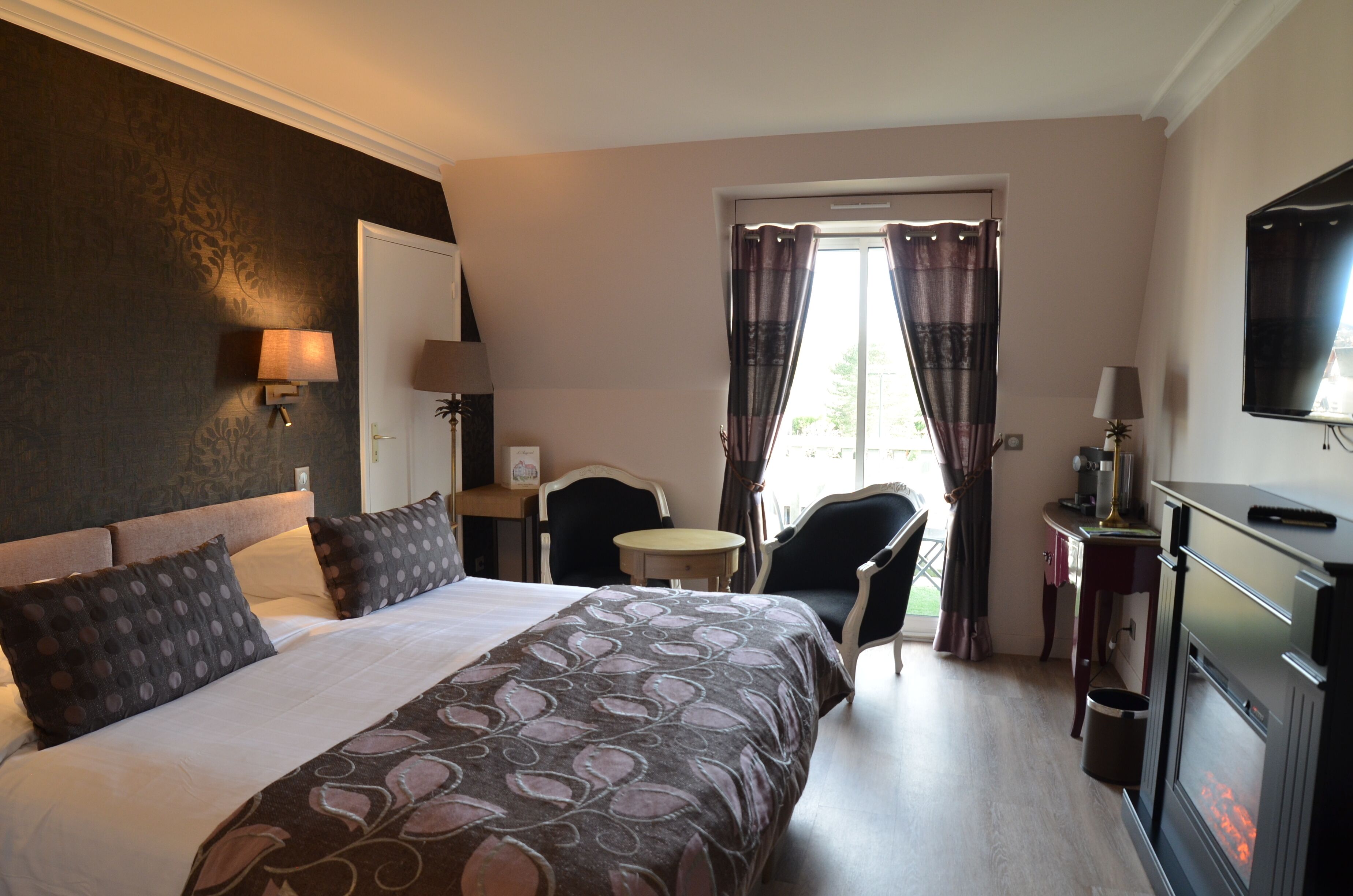 A hotel room with a large bed, a desk, a chair, a television, and a window with curtains.