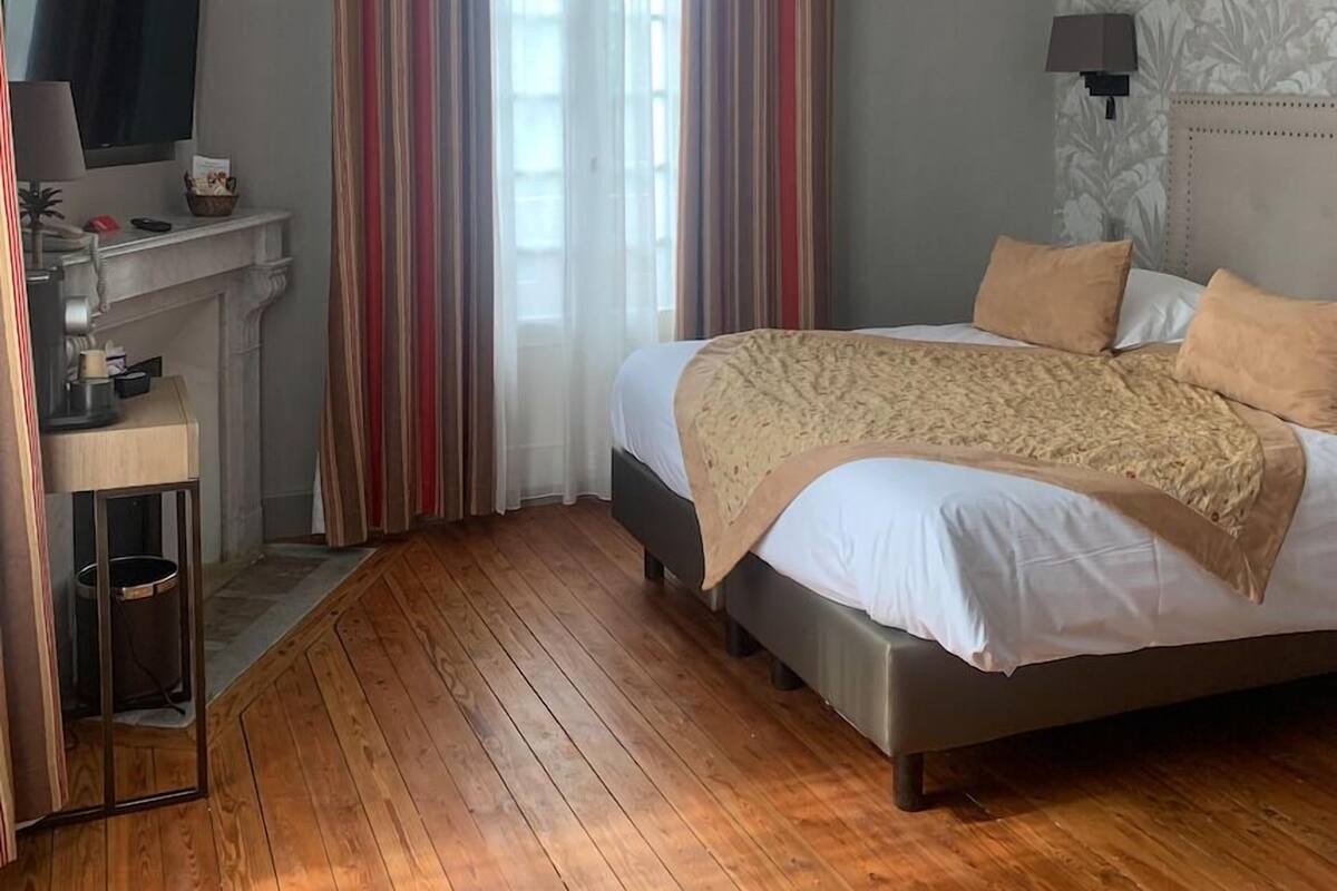 A bedroom with a bed, a TV, a desk, and a window with curtains.