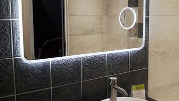 A bathroom with a white sink, a mirror with a light, and toiletries on a shelf.
