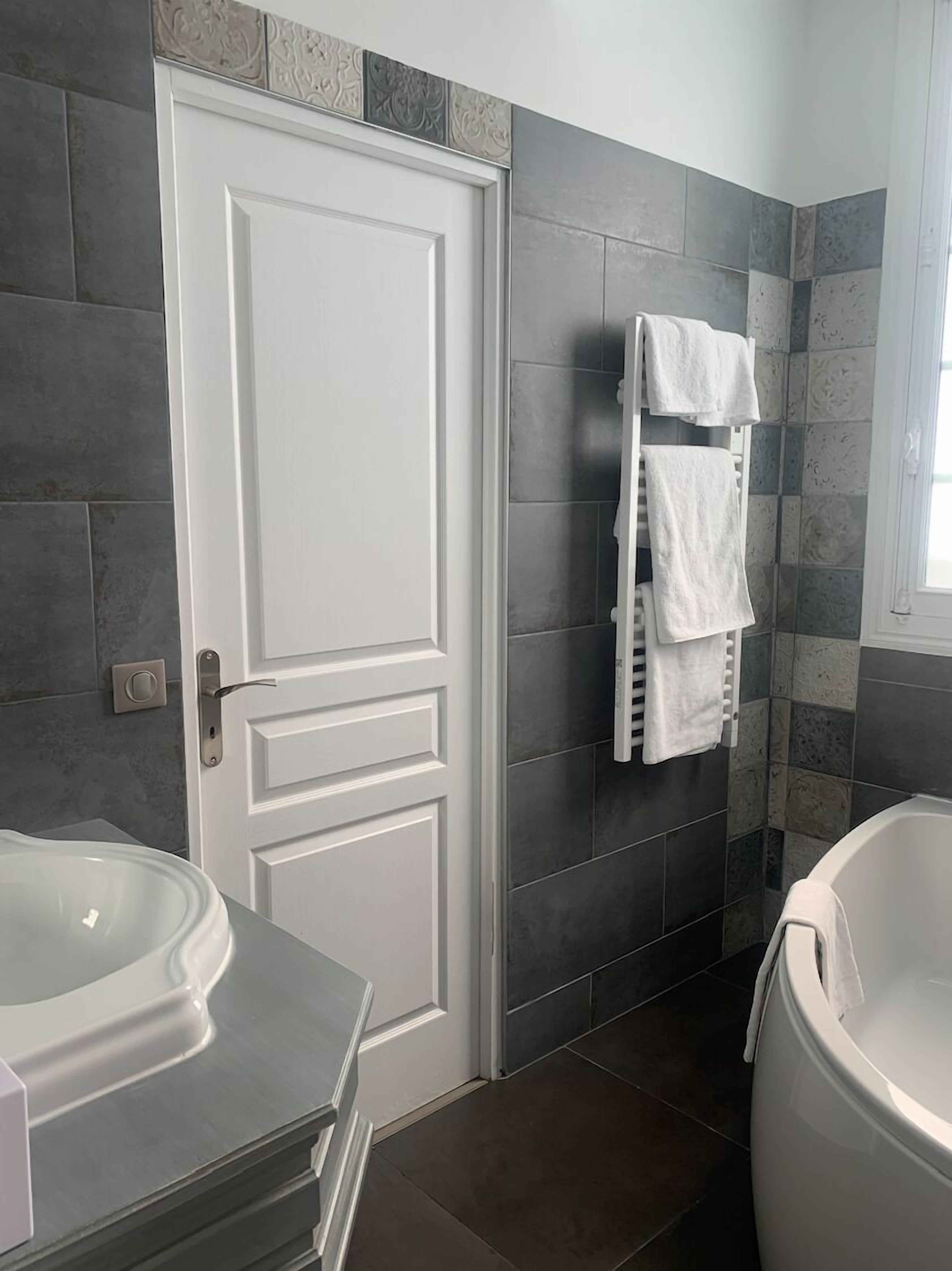 Ein Badezimmer mit weißer Tür, einem Handtuchhalter mit mehreren Handtüchern, einer Badewanne und einem Waschbecken.