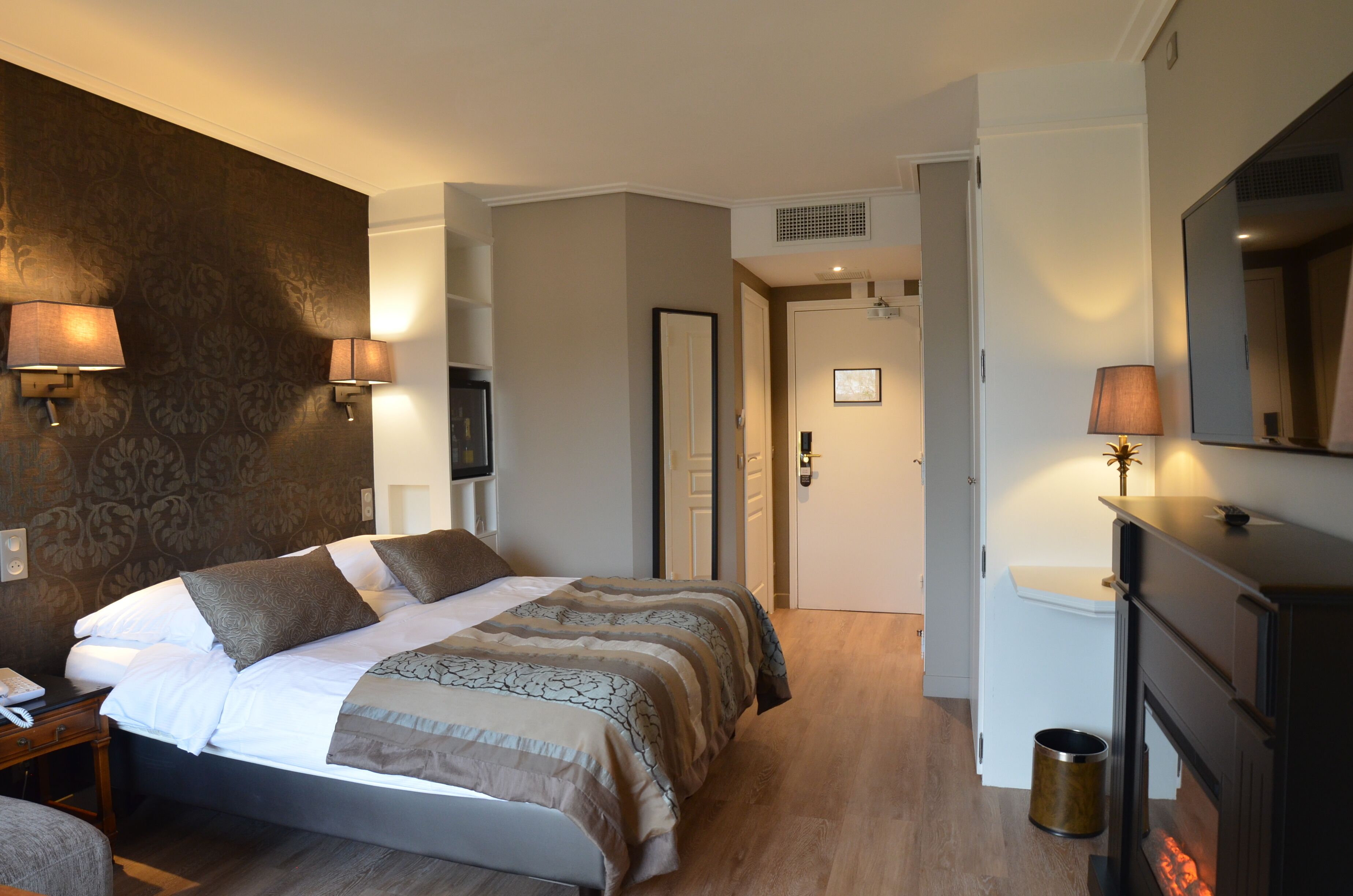 Habitación de hotel con una cama grande, dos lámparas de noche, un televisor, una chimenea y un espejo.