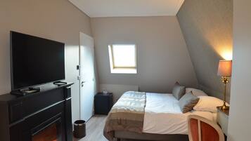 A bedroom with a TV, fireplace, bed, window, and lamp.