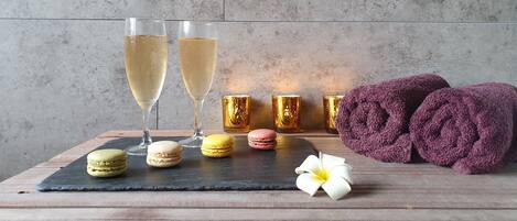 Una mesa con dos copas de champán, candelabros dorados, macarons, una toalla morada enrollada y una flor blanca.