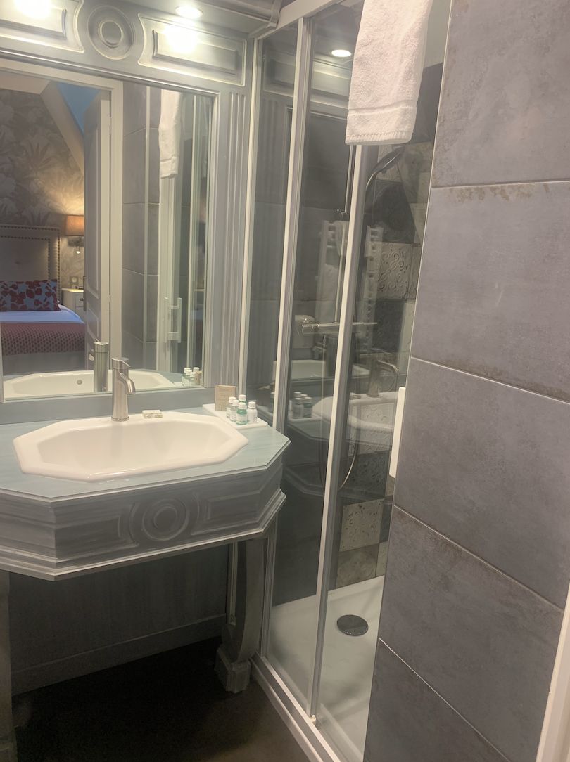 Un baño con cabina de ducha de vidrio, lavamanos con espejo y una toalla colgada en la pared.