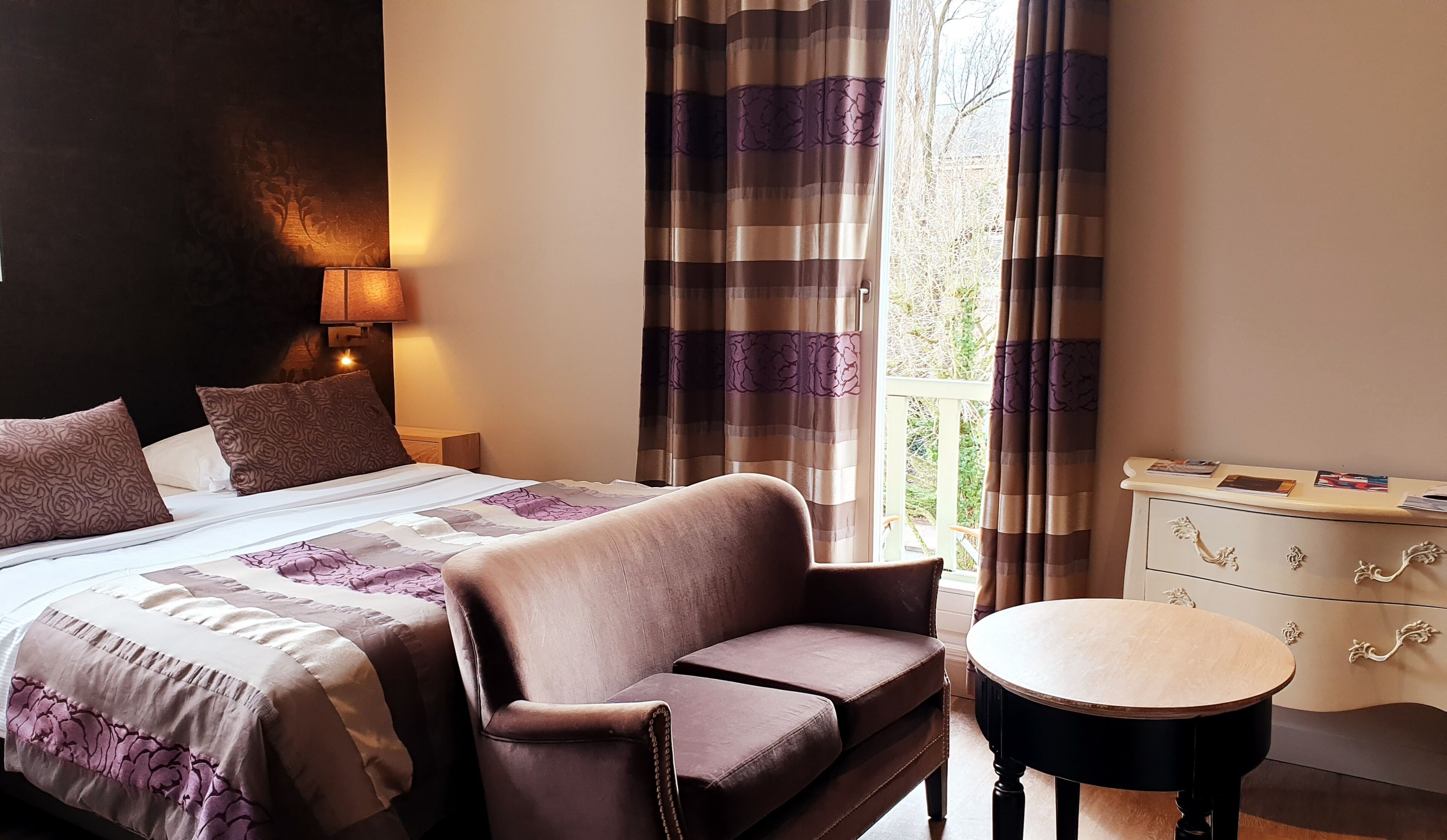 Una habitación de hotel con cama, sofá, mesa redonda y cómoda.