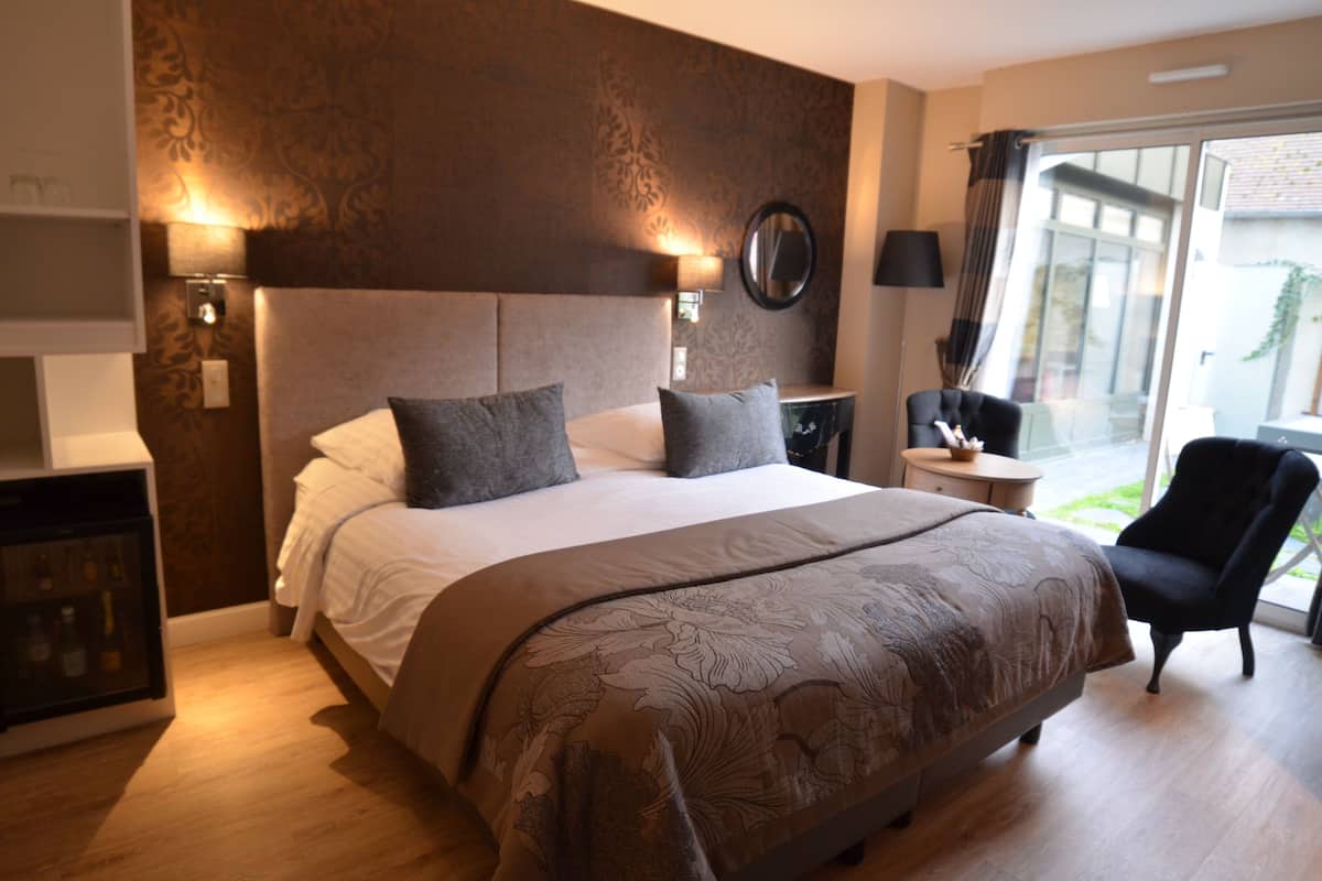 A hotel room with a large bed, a bedside table, a chair, and a view of the outdoors.