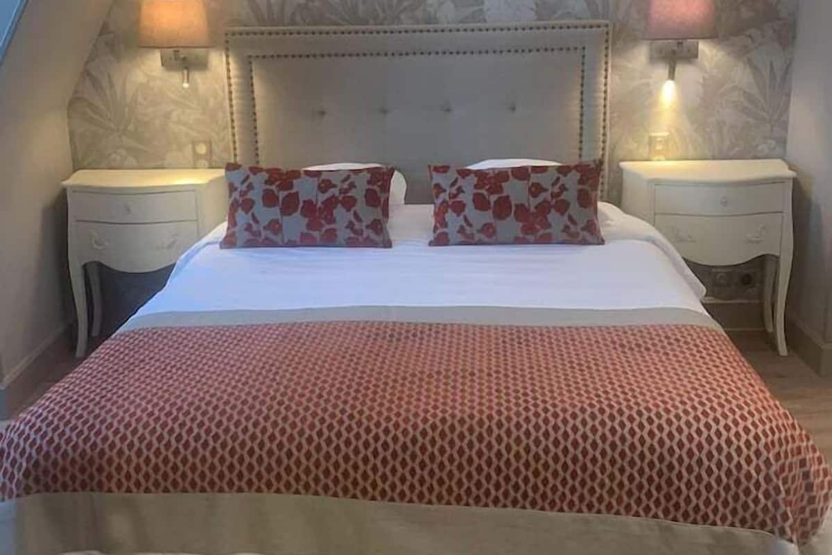 A bedroom with a large bed, floral wallpaper, two bedside lamps, and a patterned bedspread.