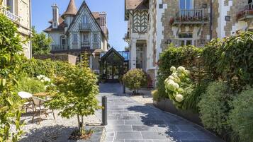 Une cour avec un chemin de pierre menant à un belvédère, entouré d’une végétation luxuriante et présentant une architecture européenne traditionnelle.