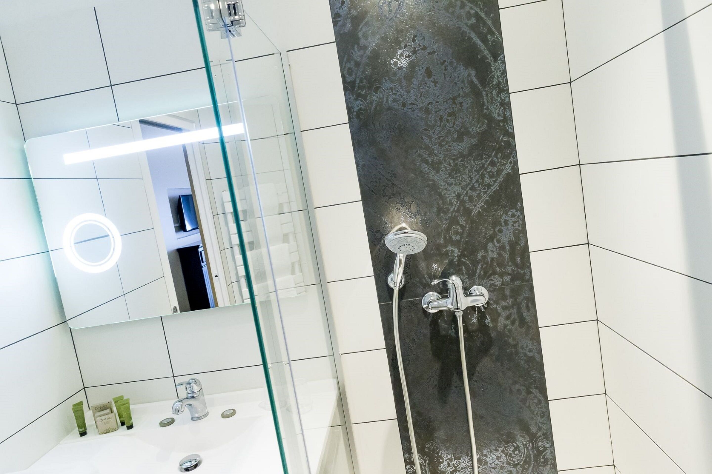 A modern bathroom with a glass shower enclosure, a large mirror, and a white sink with toiletries.