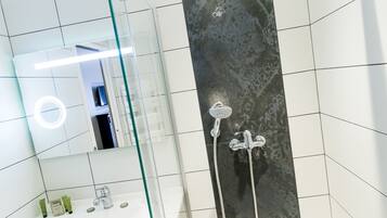 A modern bathroom with a glass shower enclosure, a large mirror, and a white sink with toiletries.