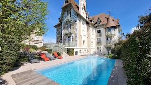 A hotel with a swimming pool, outdoor seating, and a large building with multiple balconies.