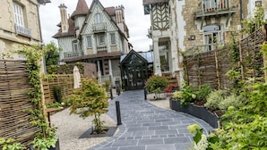 A stone pathway leading to a building with a traditional architectural style, surrounded by greenery and a wooden fence.