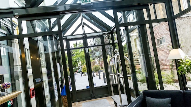 A modern hotel lobby with a glass entrance, a reception desk, and a seating area.