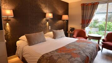 A hotel room with a large bed, two wall-mounted lamps, a chair, a small table, and a view of greenery outside.