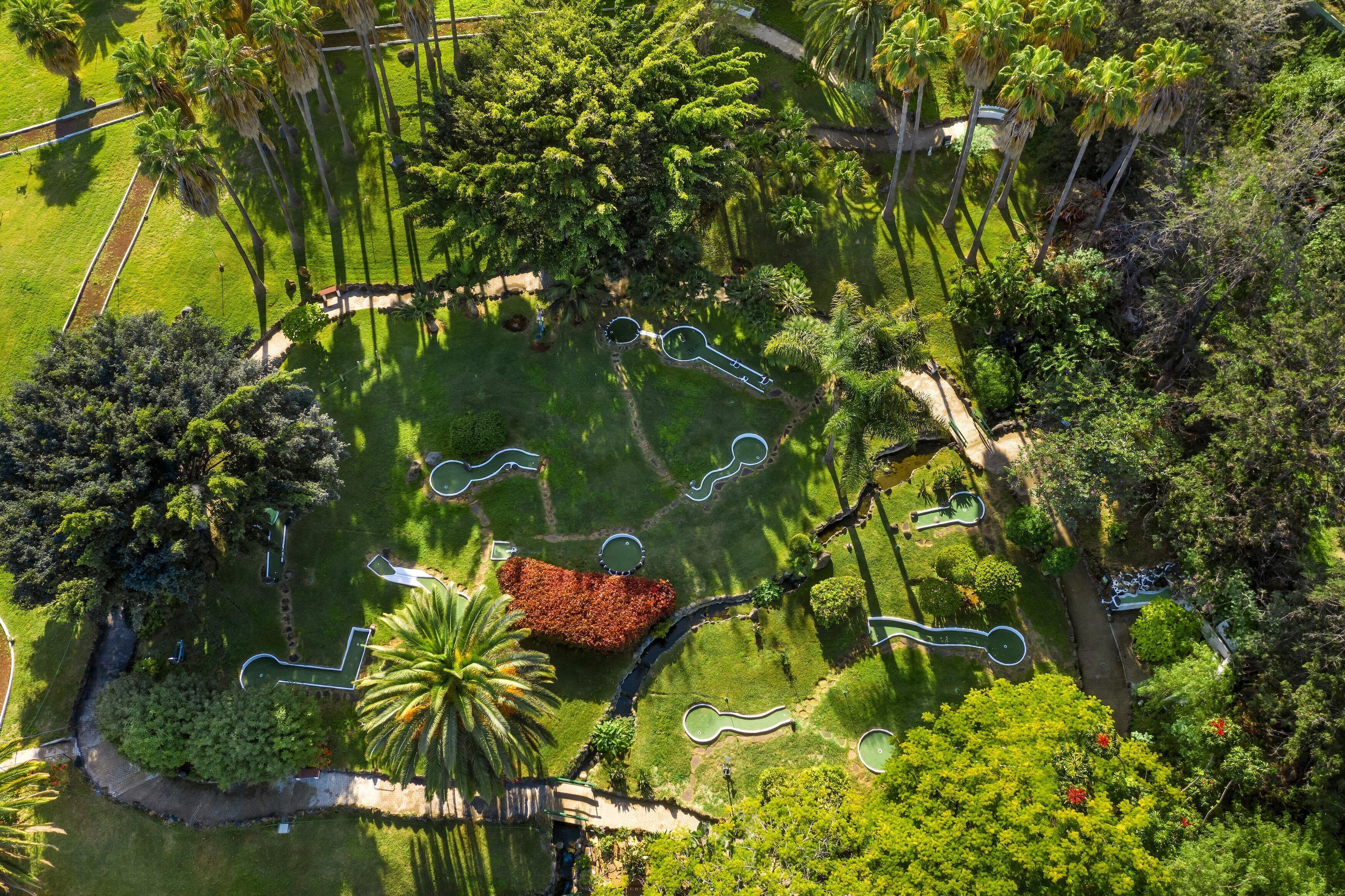 An aerial view of a park with winding pathways, palm trees, and a central red-roofed structure.