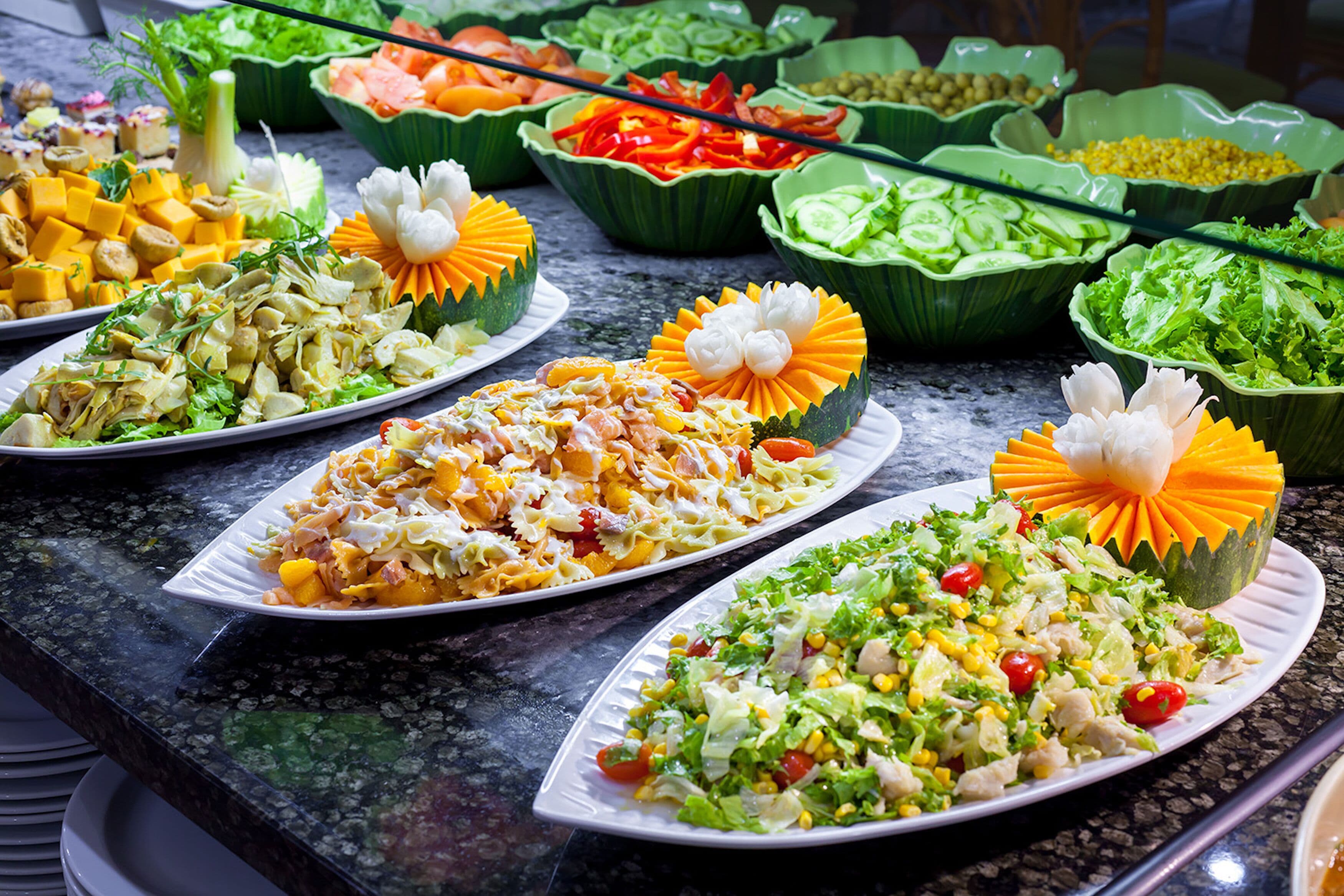 Un bufé con una variedad de platos, incluyendo ensaladas, verduras y frutas talladas.