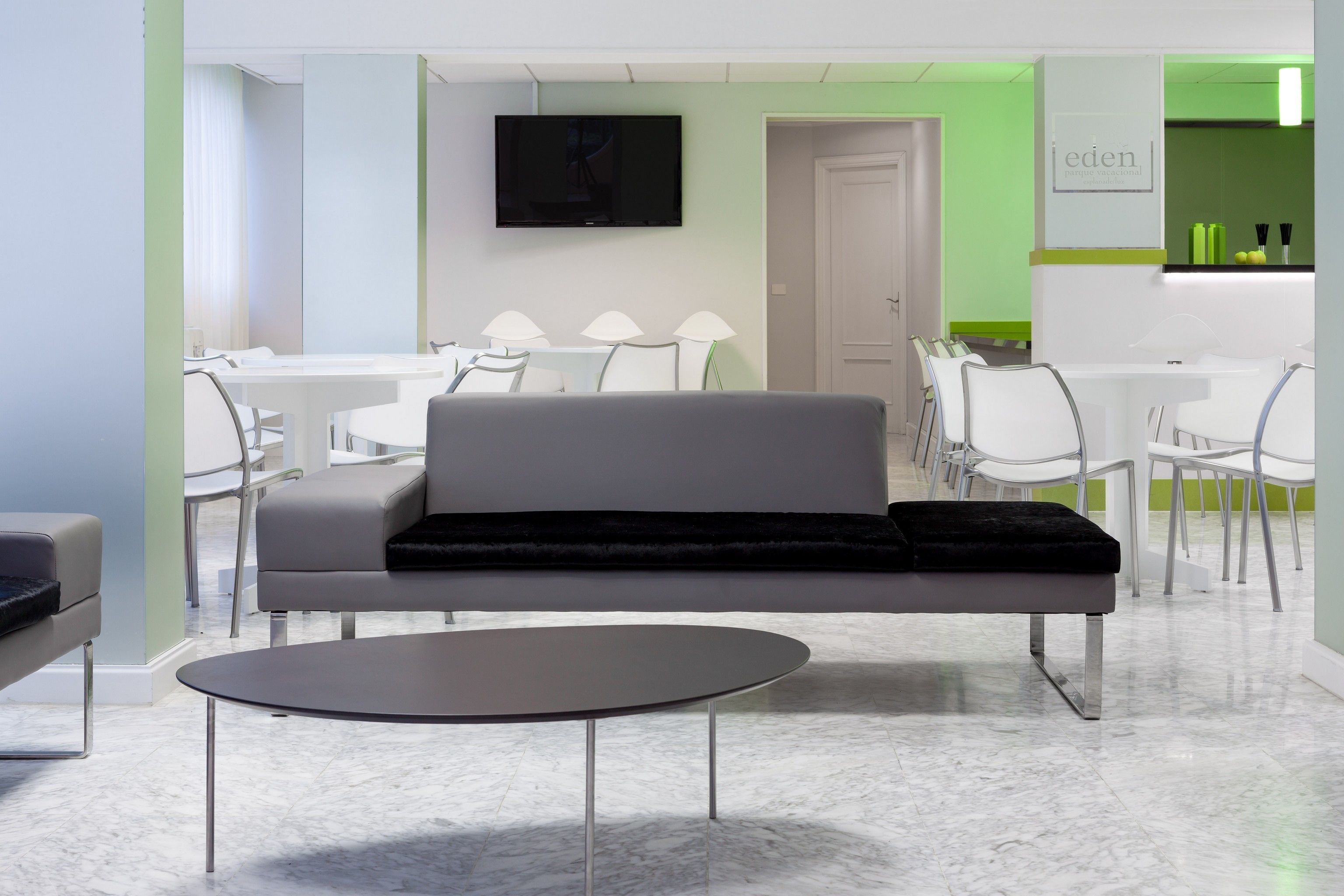 Eine moderne Hotelhalle mit grauem Sofa, einem runden Tisch und weißen Stühlen.