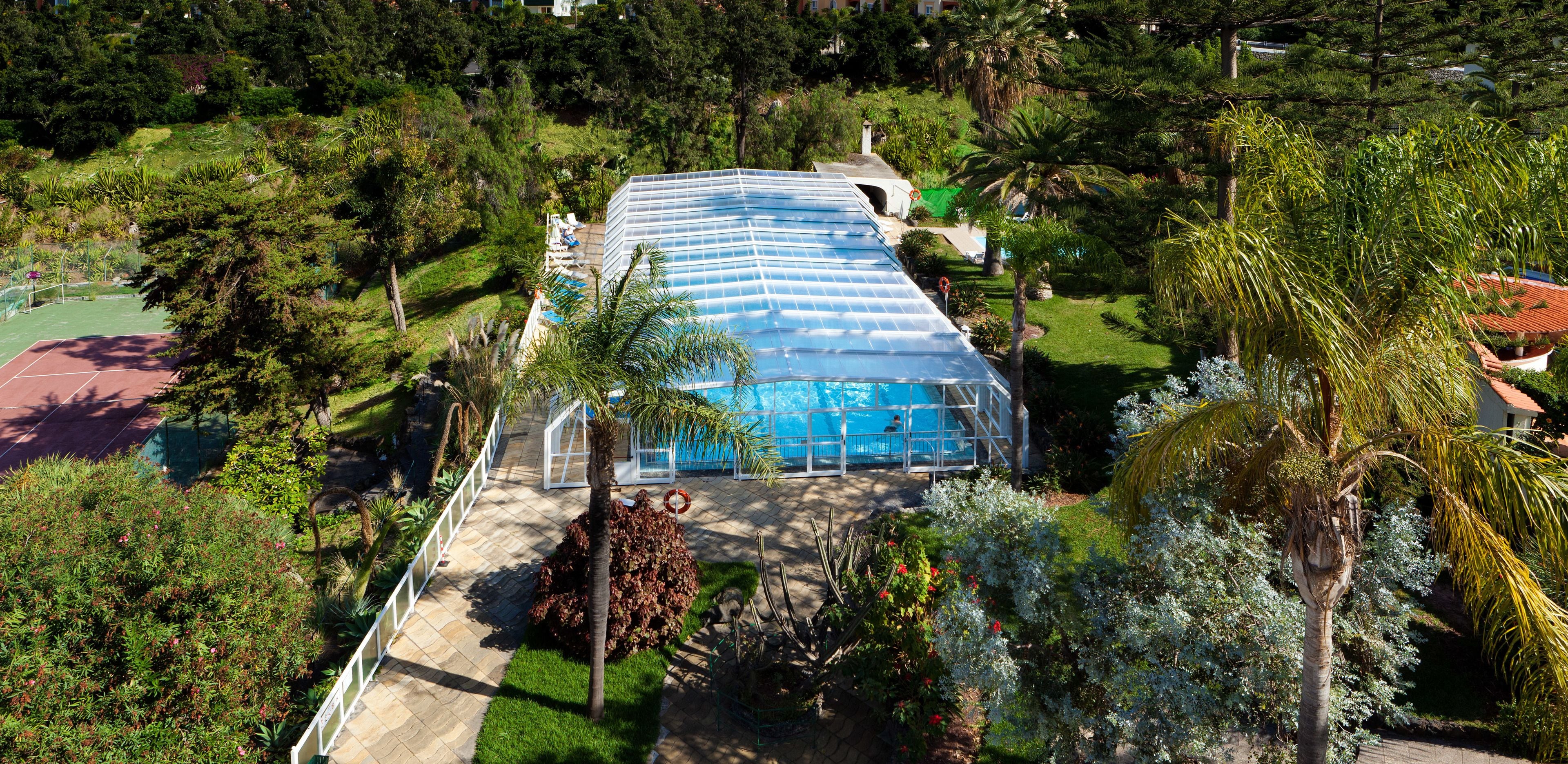 A large greenhouse structure surrounded by lush greenery and a tennis court.