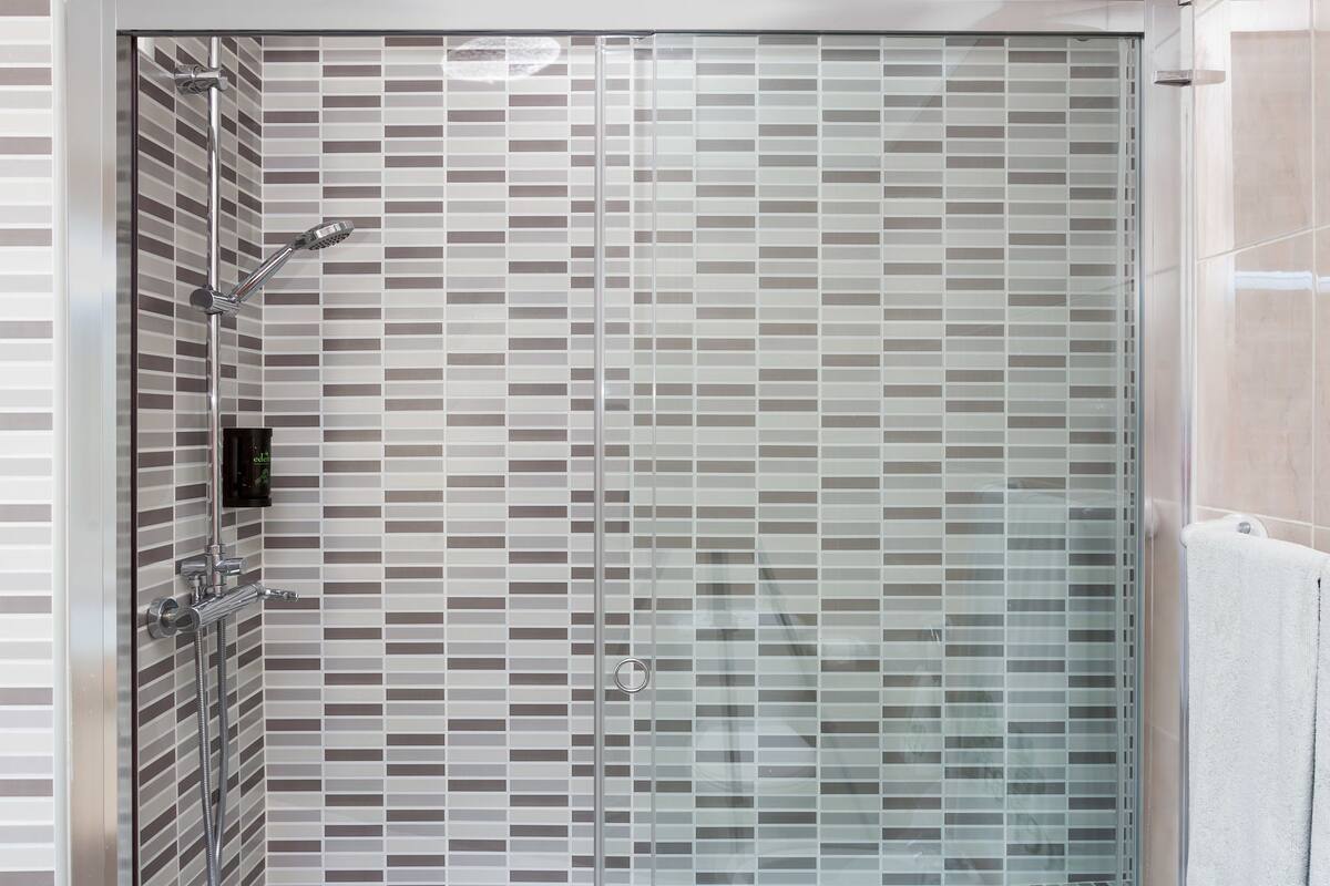Un box de ducha moderno con puerta de vidrio, cabezal de ducha de mano y panel de control.