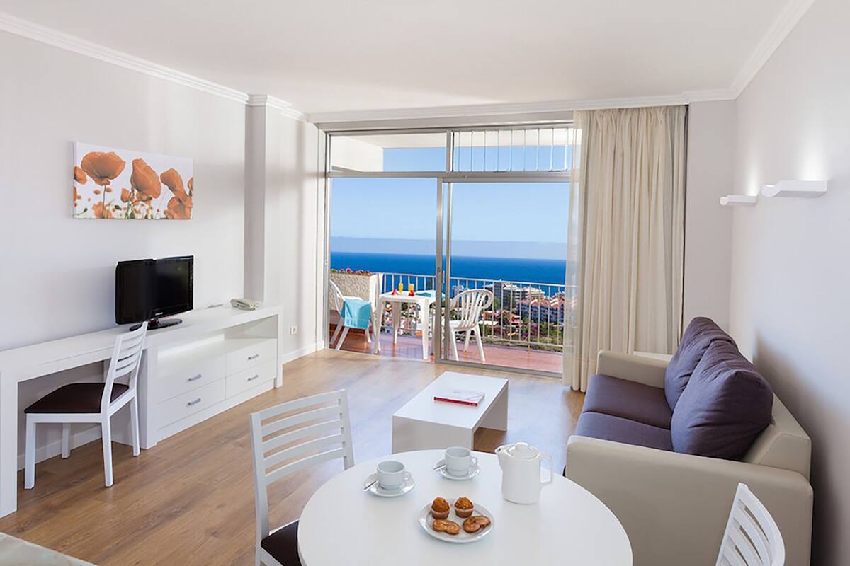 Una habitación de hotel moderna con balcón, zona de comedor y sala de estar.