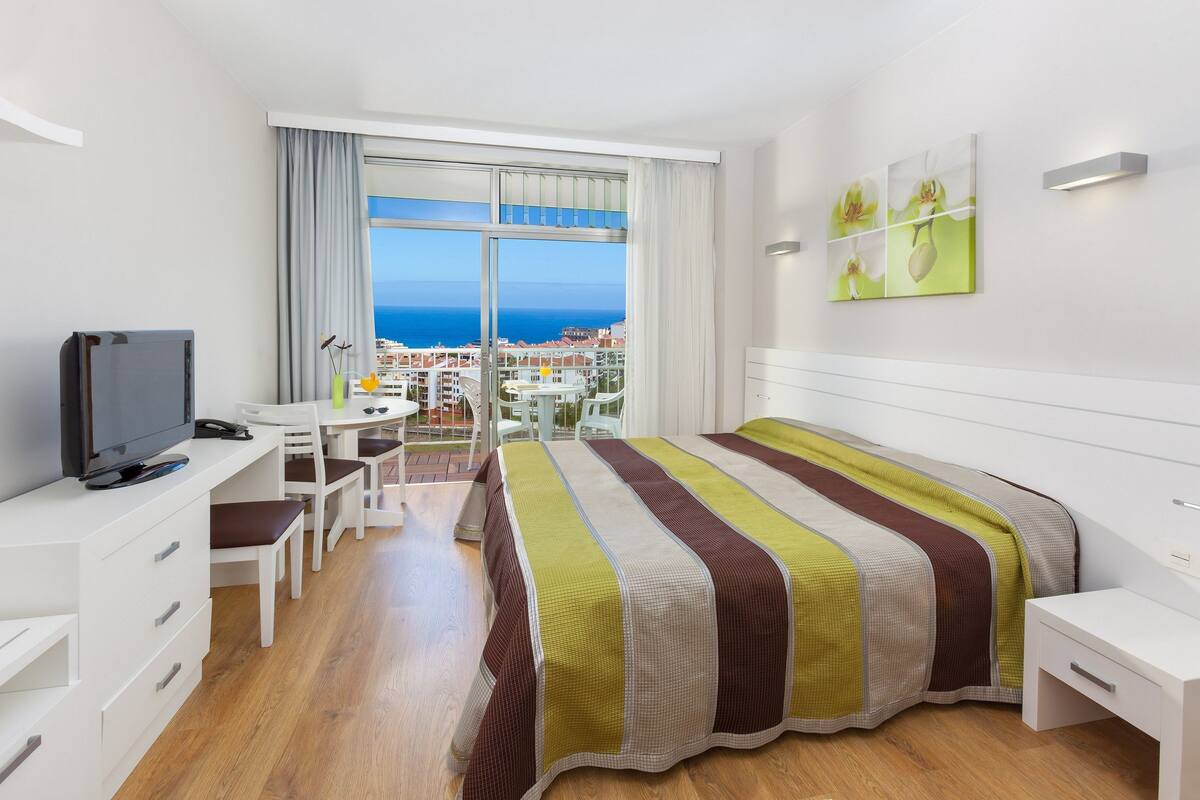 Habitación de hotel con cama, escritorio, televisor y vista al mar.