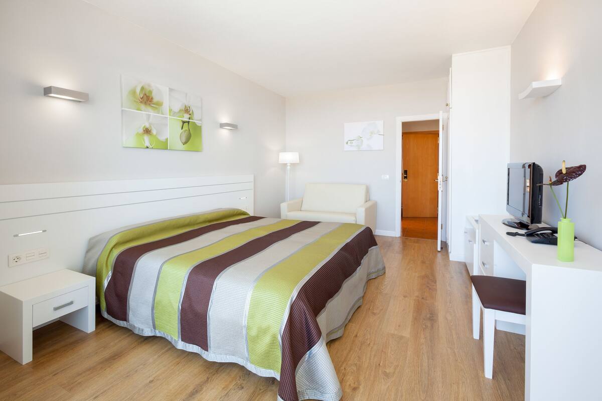 Una habitación de hotel moderna con cama, mesita de noche, escritorio, silla y televisor.