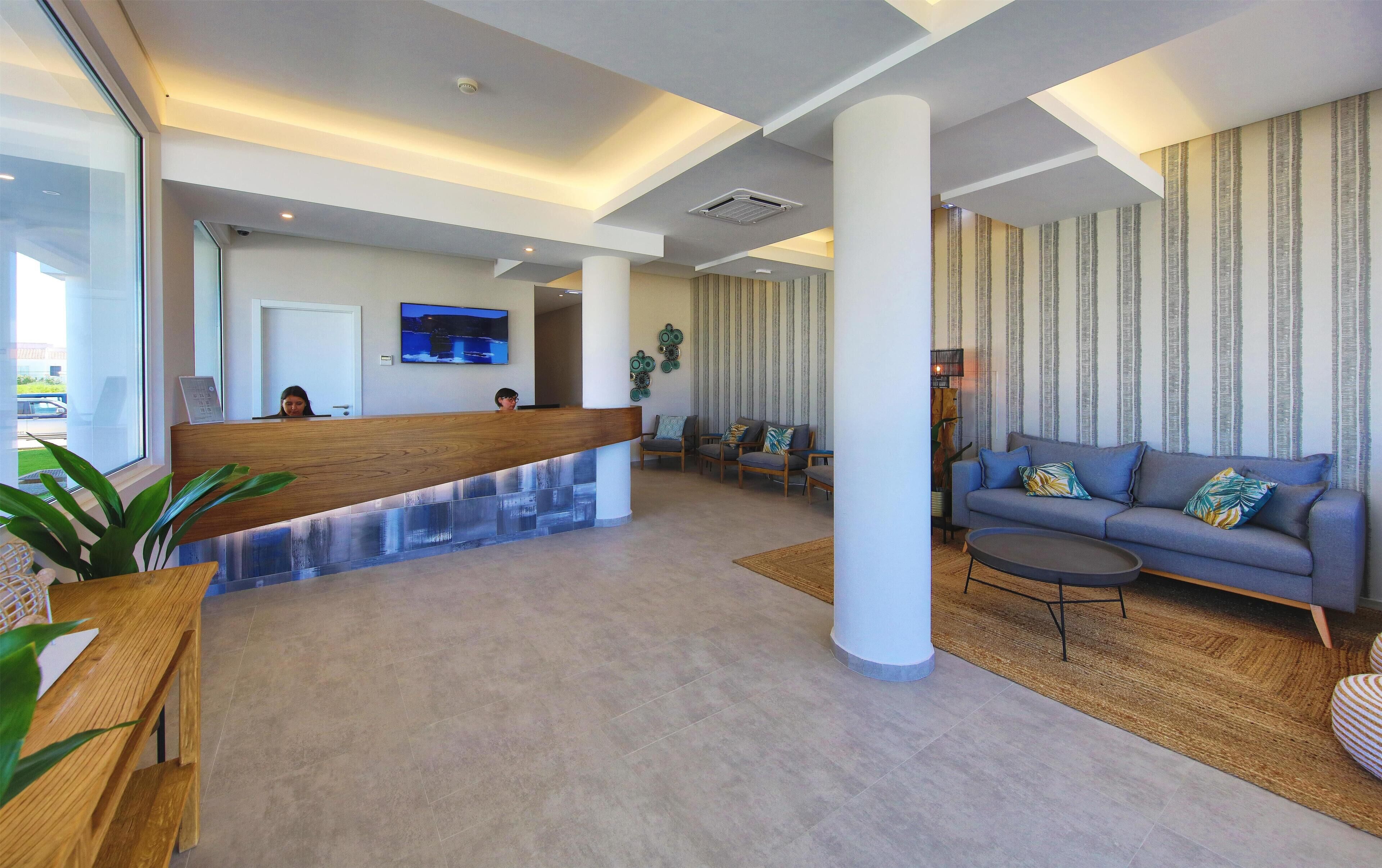 Un hall d’hôtel moderne comprenant un comptoir d’accueil, un espace salon et une grande fenêtre offrant une vue sur l’extérieur.