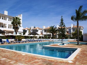 Una piscina con sillas de descanso y palmeras, rodeada de edificios con balcones.