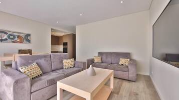 A modern living room with two grey sofas, a wooden coffee table, and a large flat-screen TV mounted on the wall.